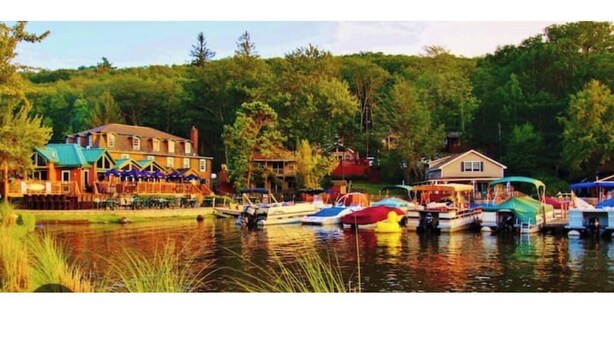A lakeside hotel with boats docked in front, surrounded by trees.