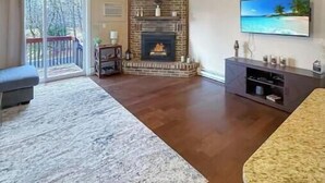 A spacious living room with a fireplace, a ceiling fan, and a large TV on the wall.