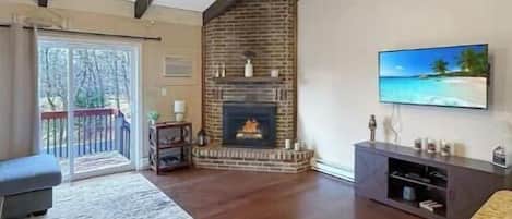 A spacious living room with a fireplace, a ceiling fan, and a large TV on the wall.