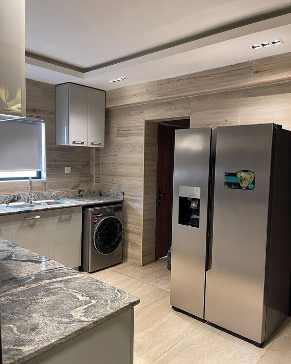 A modern kitchen with a stainless steel refrigerator, a built-in washing machine, and a marble countertop.