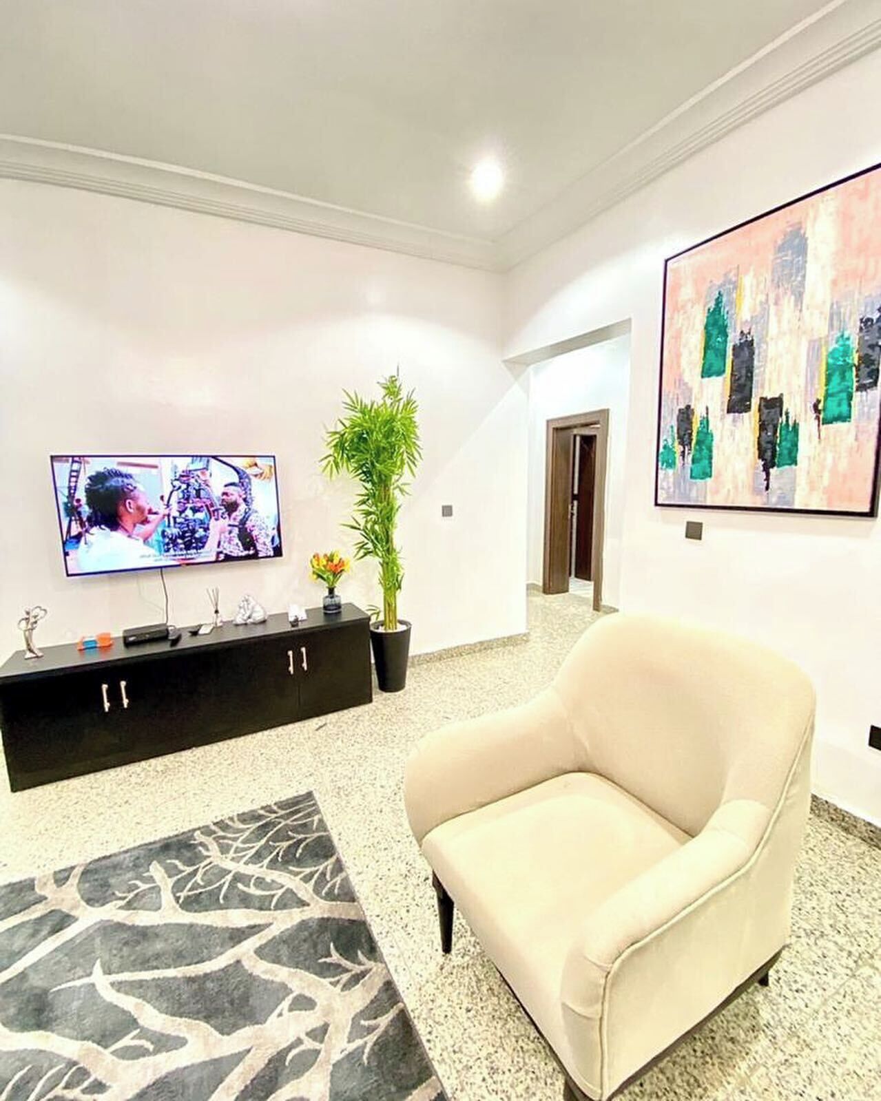 Una sala moderna con un sofá beige, un televisor de pantalla plana, un mueble de entretenimiento negro, una planta en maceta y arte abstracto en las paredes.