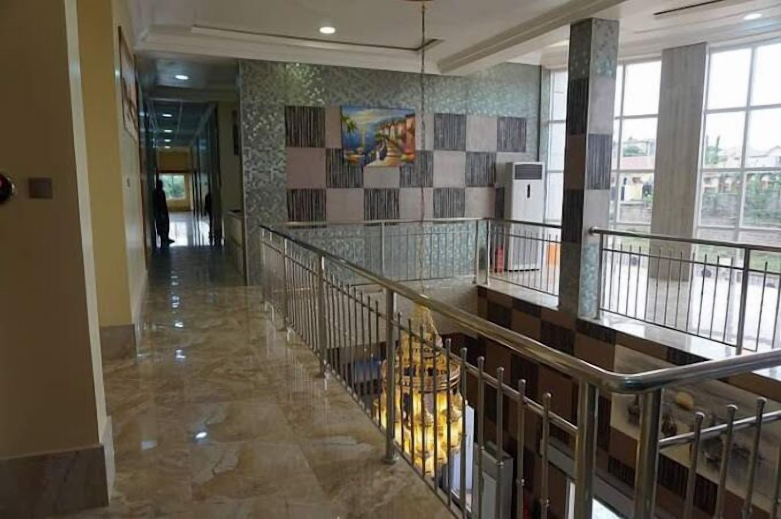 A hotel corridor with a marble floor, a staircase with metal railings, and a decorative wall with a painting.