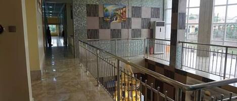 A hotel corridor with a marble floor, a staircase with metal railings, and a decorative wall with a painting.