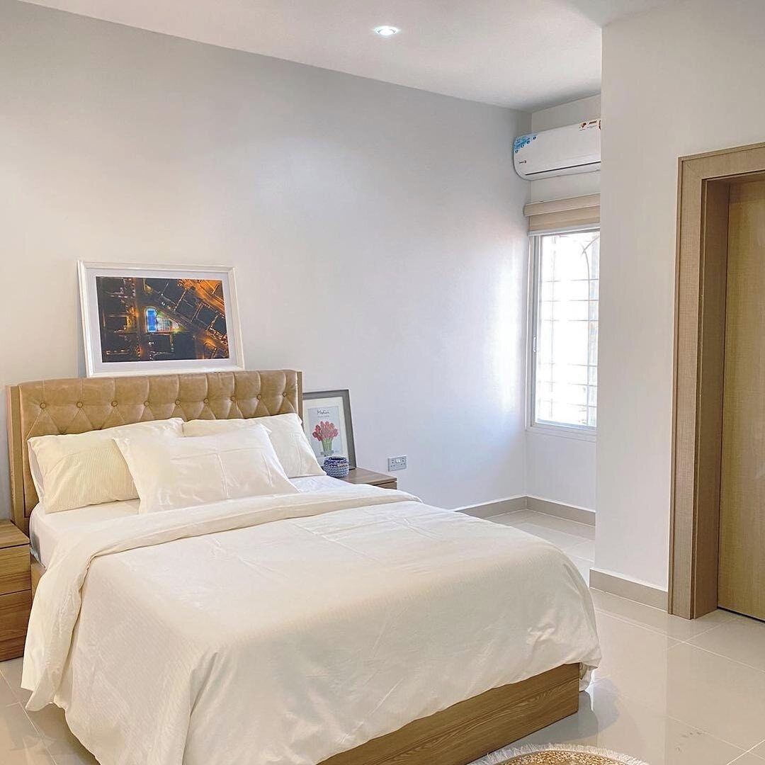 A bedroom with a large bed, a headboard, a framed picture, a nightstand, a window, and an air conditioning unit.