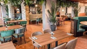 A restaurant with wooden tables and chairs, potted plants, and a stone wall in the background. - Shorefield Country Park, 3 Bed,passes Included! (Lymington)