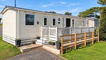A mobile home with a porch, a wooden fence, and a gravel driveway.