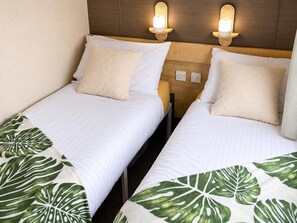 Two single beds with white bedding and green leaf-patterned throw blankets, wooden headboards, and wall-mounted reading lights. - Shorefield 3-bed Lodge, Sleeps 6 w/ Top Reviews (Lymington)