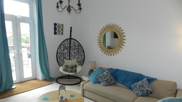 A living room with a sofa, a round coffee table, a hanging chair, a mirror, and a view through a glass door. - Troon Beachcombers Apartment (Troon)