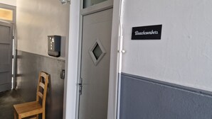 A hallway with a door labeled "Beachcombers," a wooden chair, a security keypad, and a small window. - Troon Beachcombers Apartment (Troon)