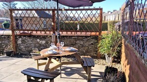 An outdoor patio with a round wooden table set for two, a bench, and a small umbrella. - Troon Beachcombers Apartment (Troon)