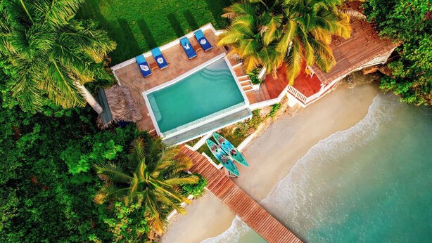 Vista aérea de un resort con piscina, playa y muelle de madera.