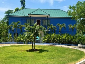 A blue building with a green roof, surrounded by a well-maintained lawn and palm trees. - Award-winning villa with private beachfront and pool (Culloden White House)