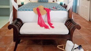 Una cama con dosel, una mesita de noche con lámpara y una cesta de toallas.