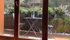 A patio area with a table and chairs, surrounded by potted plants and a view of a forested area.