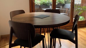 A round wooden table with four chairs, a black placemat, and a view of an outdoor patio with plants and a railing.