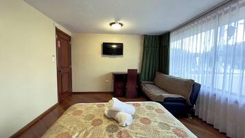 Habitación de hotel con cama, escritorio, silla, televisión y ventana con cortinas.