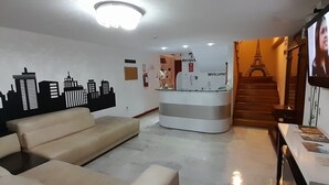 Una zona reception con un murale che raffigura una vista cittadina, una scrivania, un divano e una scala che conduce a un piano superiore.