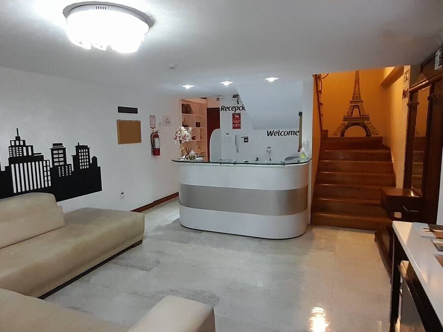 A reception area with a cityscape wall, a reception desk, a sofa, and a staircase leading to an upper floor.