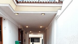 Un ampio patio con pavimento piastrellato, una zona coperta con tetto e vista su un edificio sullo sfondo.