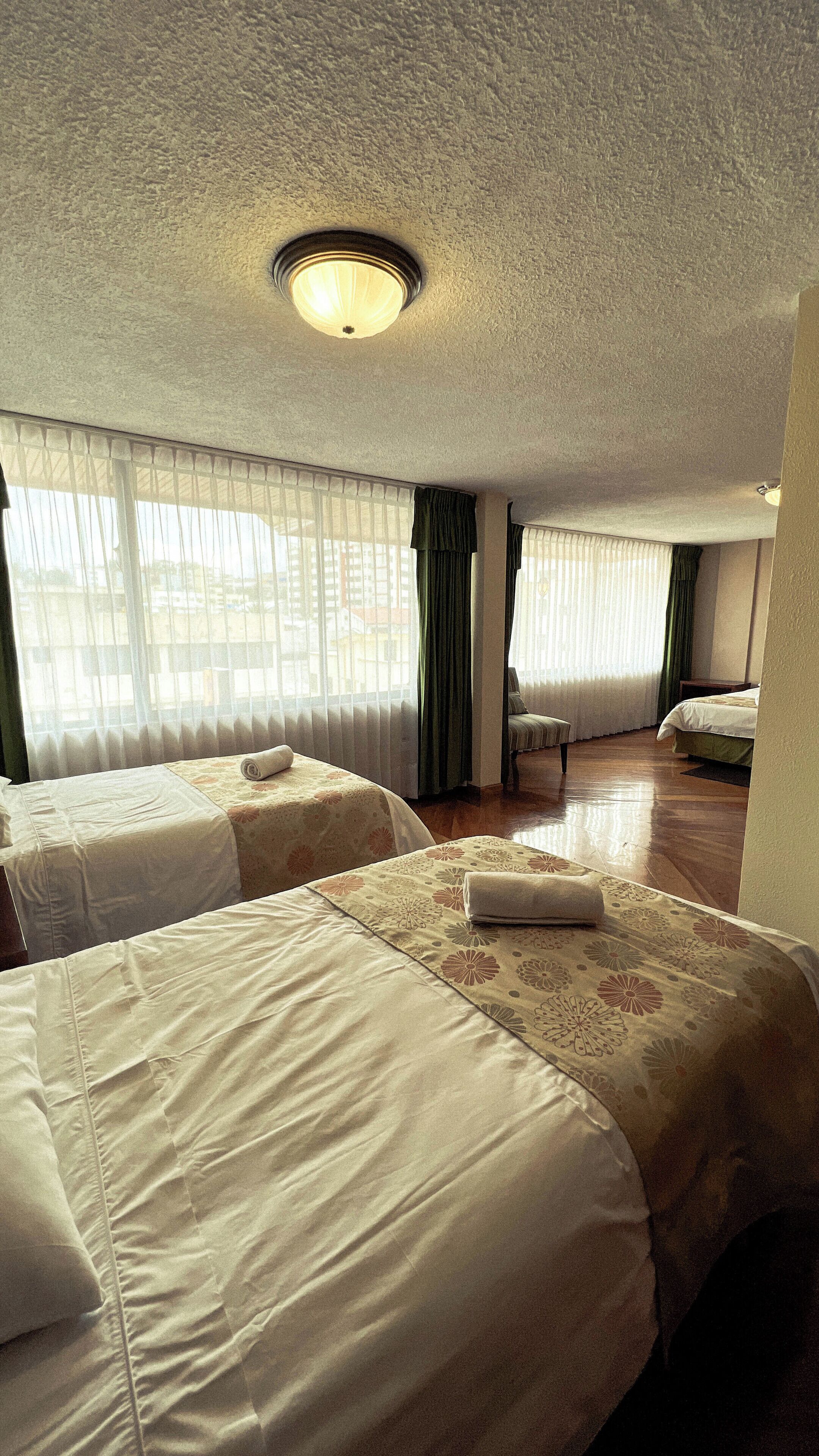 A hotel room with two beds, a chair, and a large window with curtains.