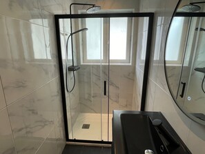 A modern bathroom with a glass-enclosed shower, a black countertop, and a large mirror.