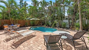 Quintal com piscina, móveis de varanda e plantas tropicais exuberantes.