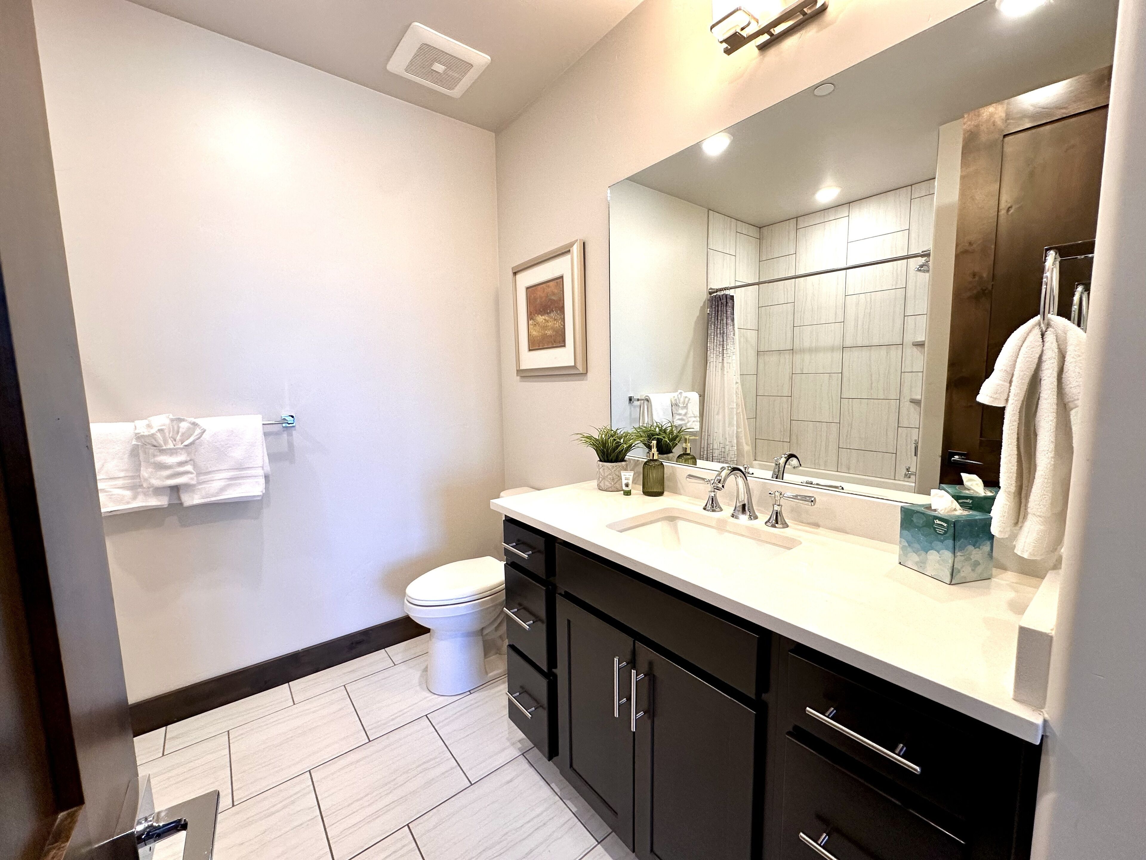 A modern bathroom with a white sink, black cabinets, a large mirror, and a toilet.