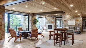 Un vaste espace de vie agrémenté d’une cheminée en pierre, de meubles en bois et de grandes fenêtres offrant une vue sur l’extérieur.
