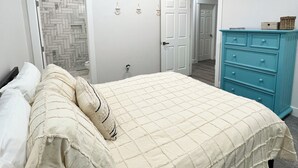 Une chambre à coucher comprenant un lit, une commode et une porte donnant sur une autre pièce.