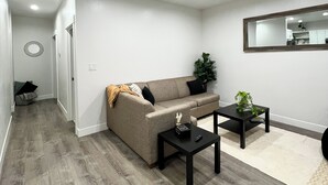 Un salon moderne avec un canapé, une table basse et une petite table d’appoint. Un miroir est accroché au mur et une plante est posée sur la table d’appoint.