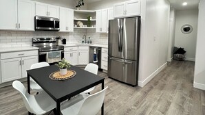 Une cuisine moderne avec des meubles blancs, des appareils en acier inoxydable et un coin repas comprenant une table noire et des chaises blanches.