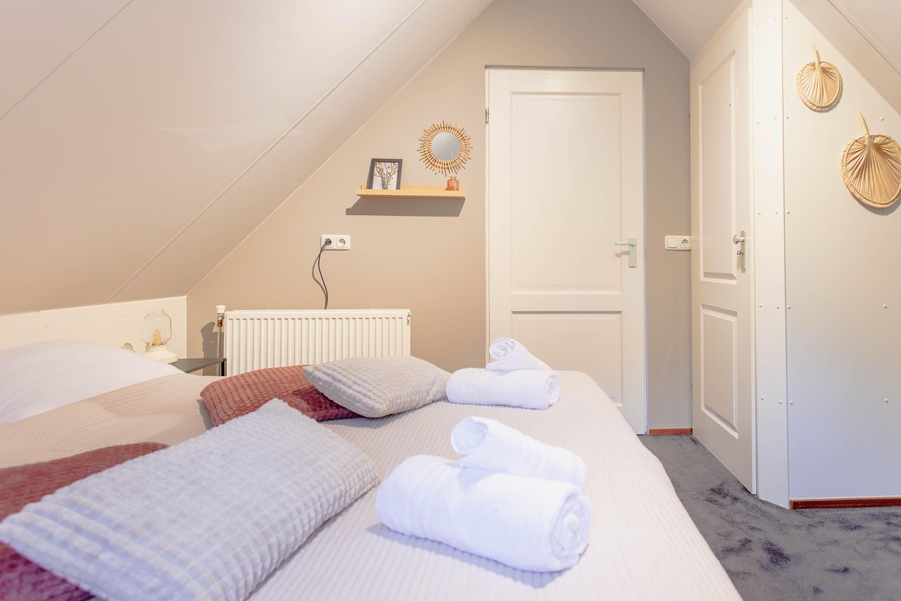 A bedroom with a bed, towels, a radiator, a door, and wall decorations.