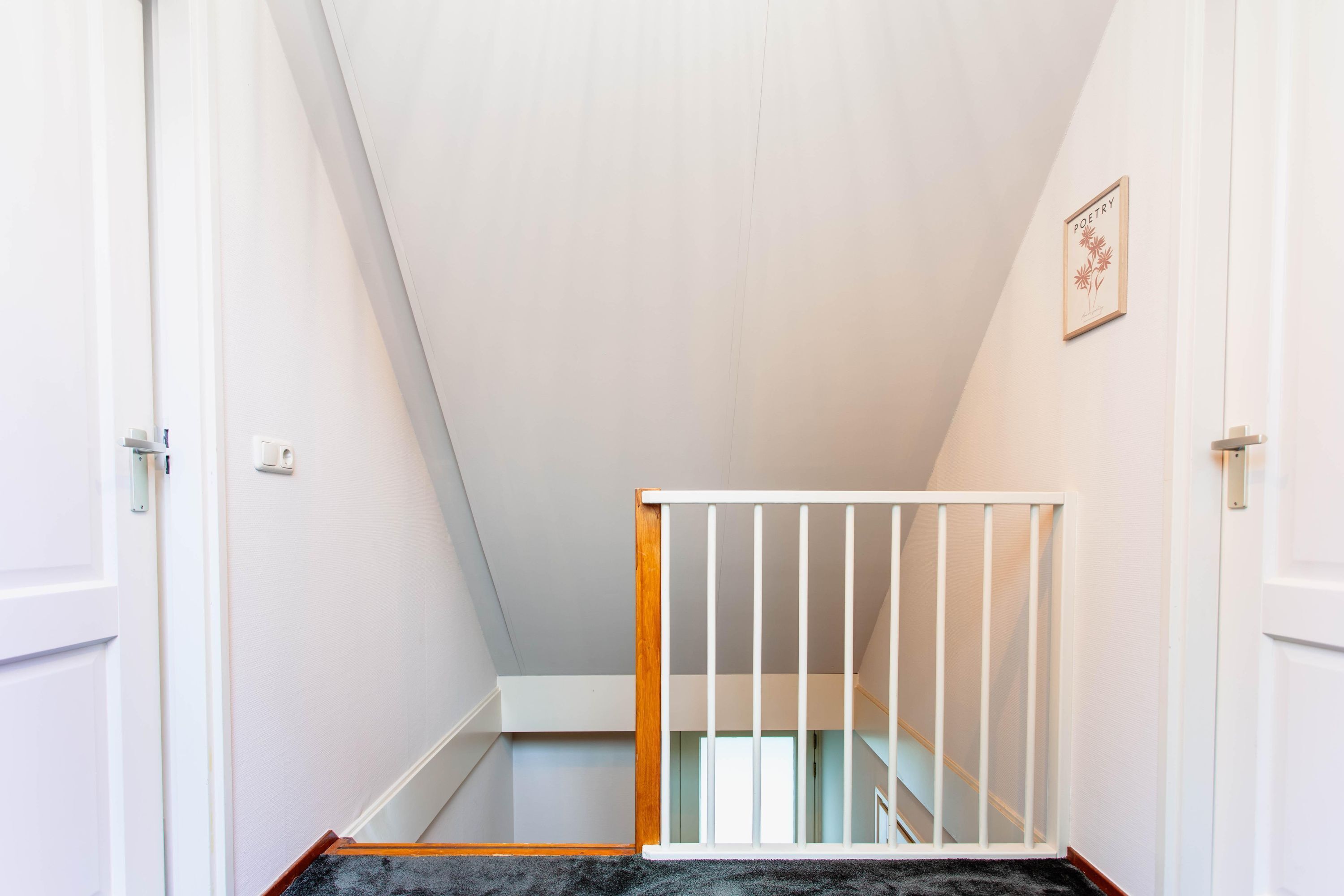 Un escalier étroit avec une rampe blanche, une main courante en bois et une porte blanche sur le côté gauche.
