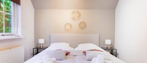 A neatly made bed with white linens and towels, two bedside tables with lamps, and a wall with three circular wall art pieces.