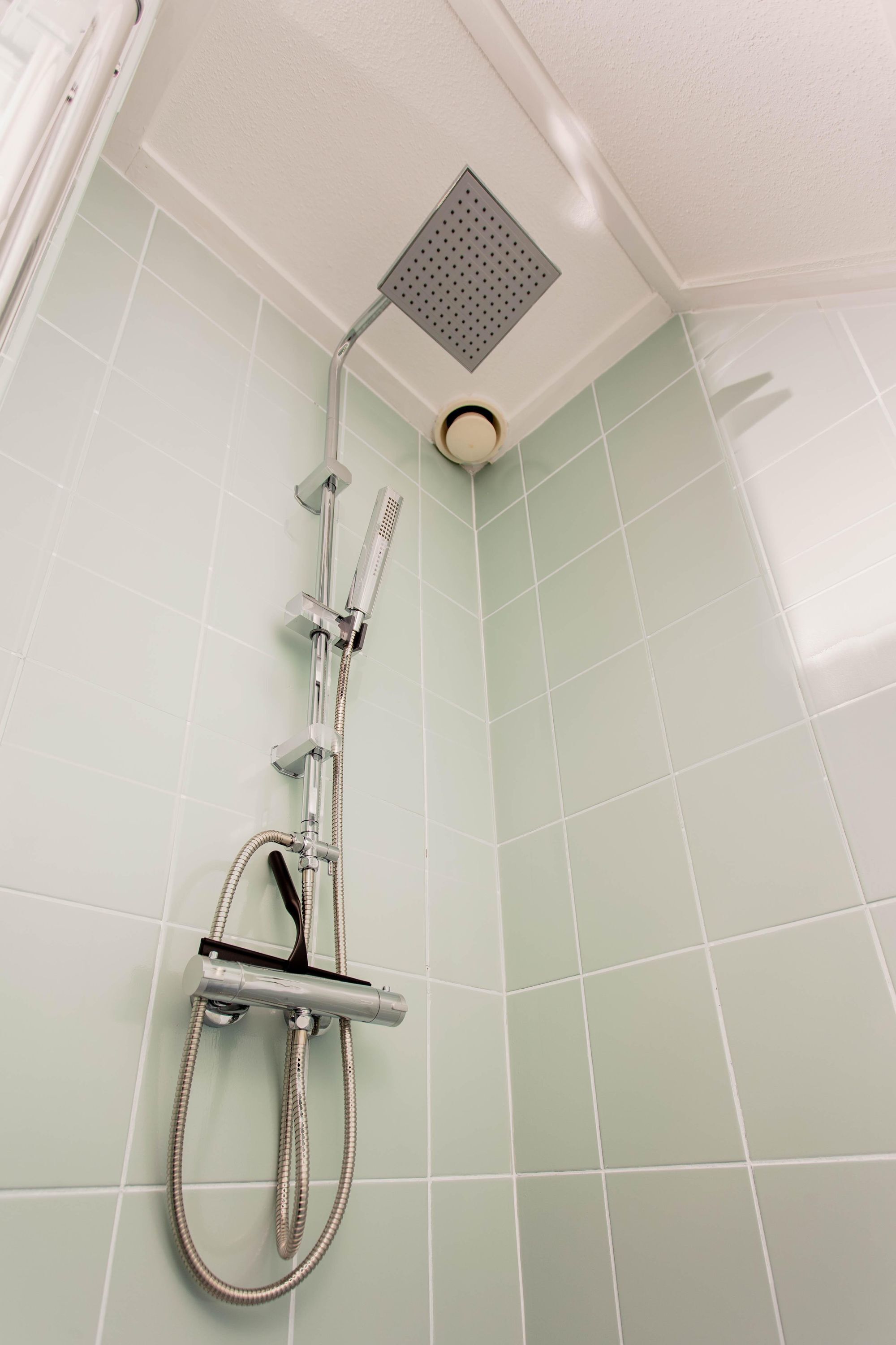 A shower with a handheld showerhead and a fixed overhead showerhead, both mounted on a wall with light green tiles.