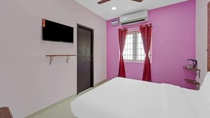 Un dormitorio con una cama, ventilador de techo, unidad de aire acondicionado, televisor montado en la pared y una ventana con cortinas rojas.