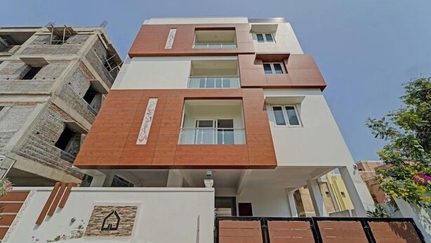 Un edificio residencial de varios pisos con un diseño moderno, que presenta una combinación de paneles exteriores blancos y marrones, varios balcones y una entrada con portón.