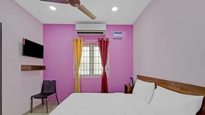Un dormitorio con cama, una silla, televisión, aire acondicionado y ventana con cortinas.