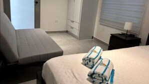 A hotel room with a bed, a sofa, a wardrobe, and a window with blinds.