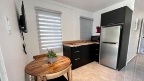 A modern kitchen with a wooden dining table, black cabinets, and a stainless steel refrigerator.