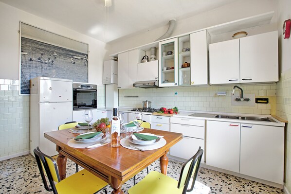 Una cocina con armarios blancos, una mesa de comedor de madera, sillas y un respuesto de azulejos.