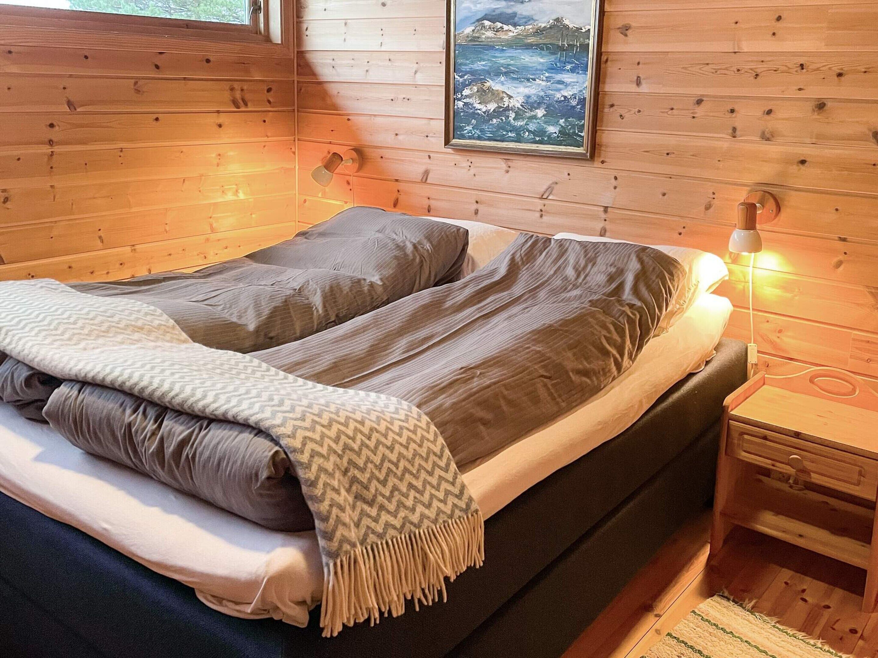 Quarto de cabana de madeira com uma cama, uma mesinha de cabeceira e um quadro na parede.