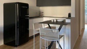 A compact kitchen with a black refrigerator, white cabinets, and a dining area with two chairs.