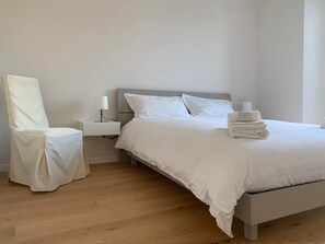 Een slaapkamer met een bed, een stoel, een nachtkastje en een lamp.