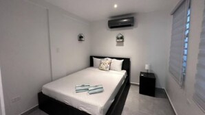 Une chambre à coucher comprenant un lit, une table de chevet, un appareil de climatisation et une fenêtre avec des stores.
