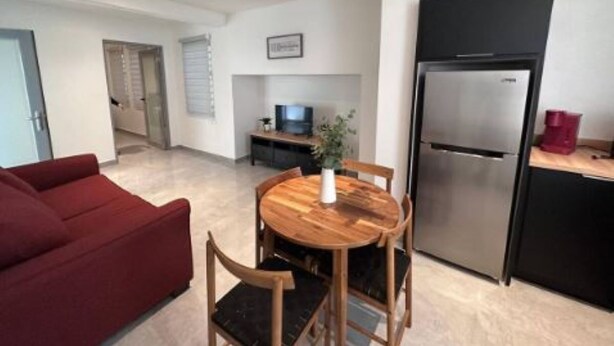 Une cuisine moderne avec un réfrigérateur en acier inoxydable, une table à manger avec des chaises en bois et un canapé rouge dans un salon lumineux.