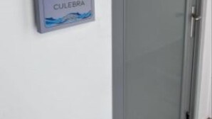 Une porte sur laquelle est apposée une plaque portant l’inscription « CULEBRA », le tout sur un mur blanc.