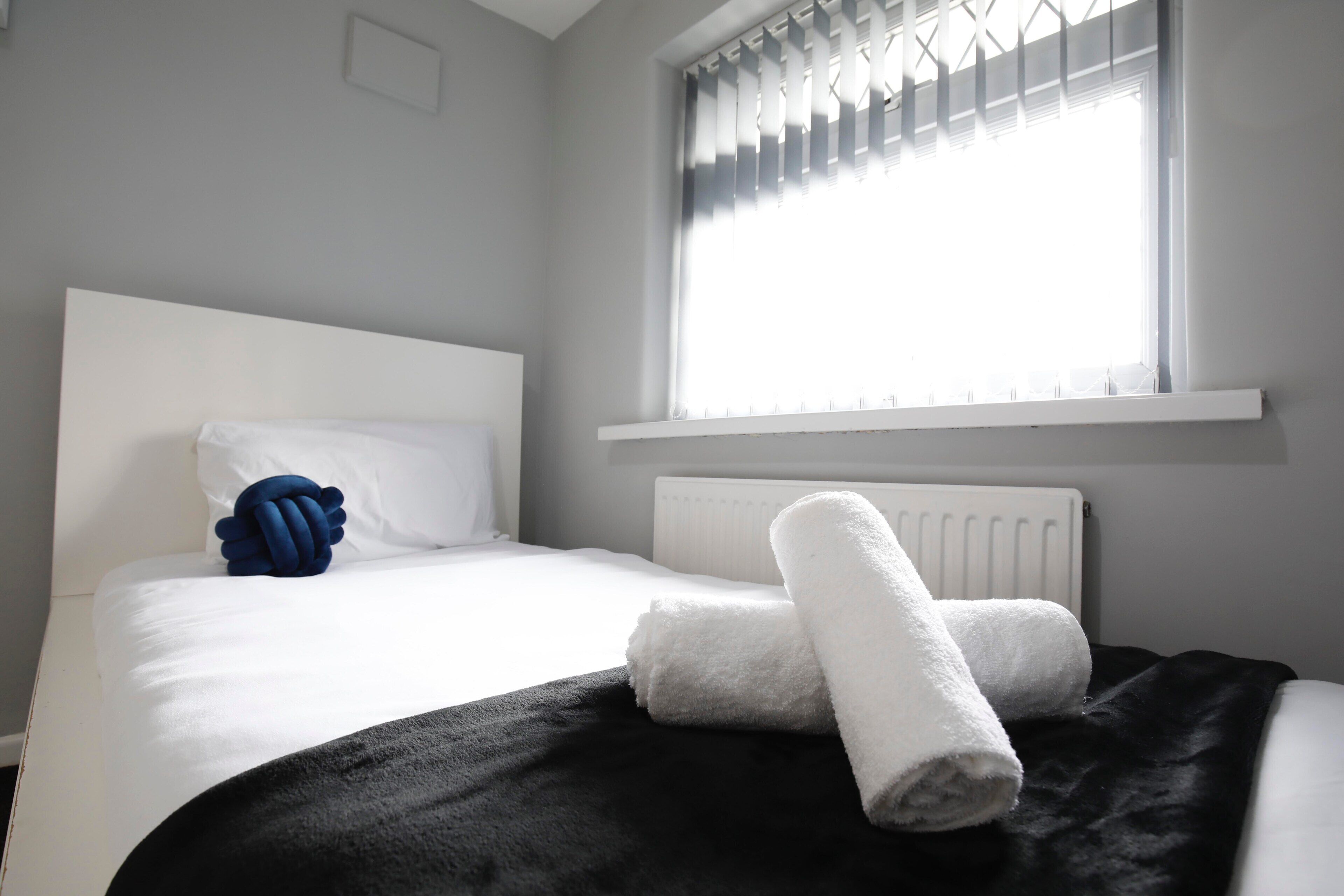 A neatly made bed with white and black bedding, a blue decorative pillow, and a white towel.