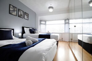 Habitación de hotel moderna con dos camas, un espejo grande y vistas al exterior a través de amplios ventanales.