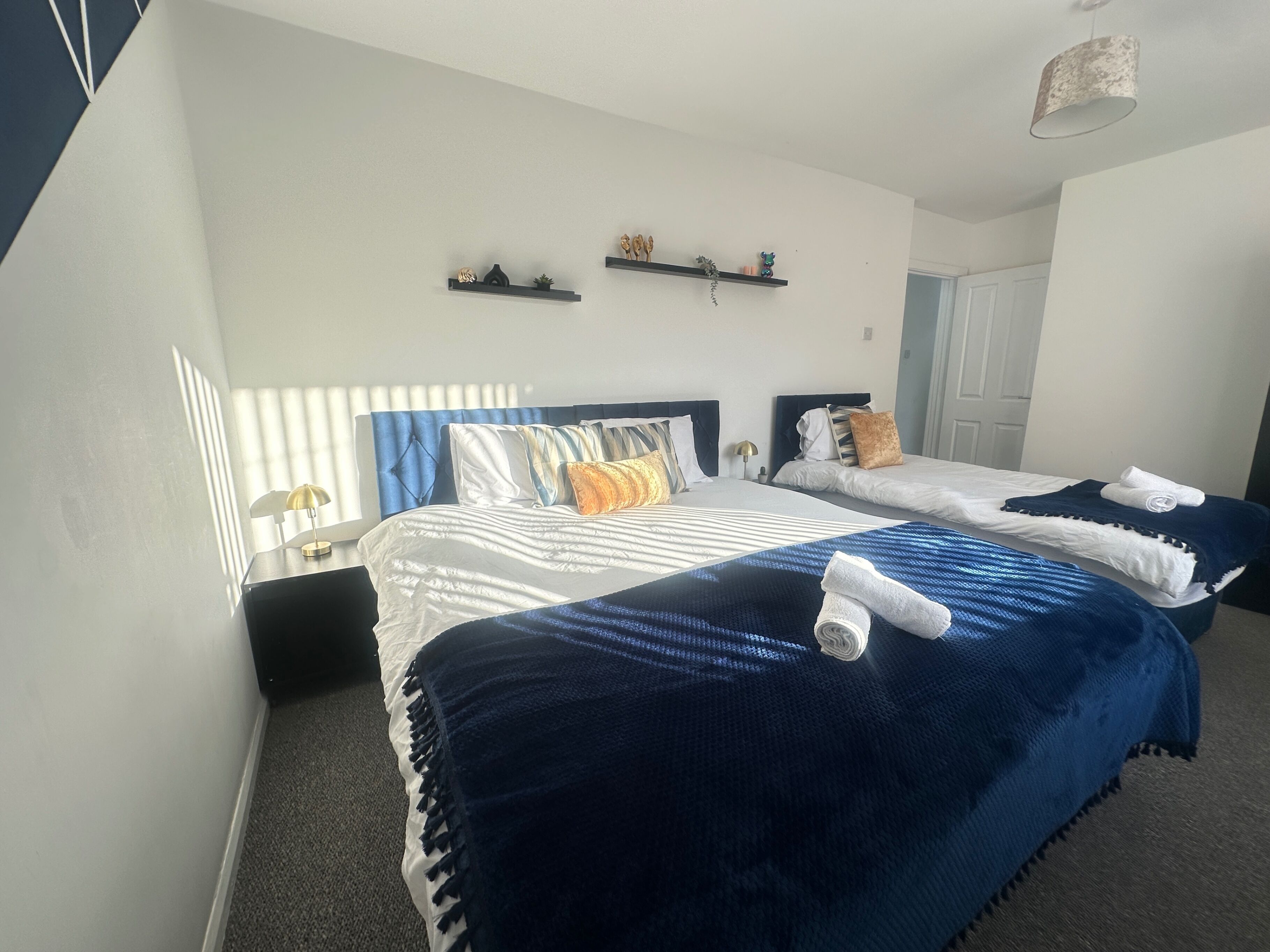 A hotel room with two beds, a nightstand, a lamp, and a ceiling light.